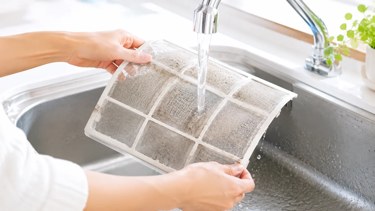 エアコンのフィルターを取り外して水洗いしている手元