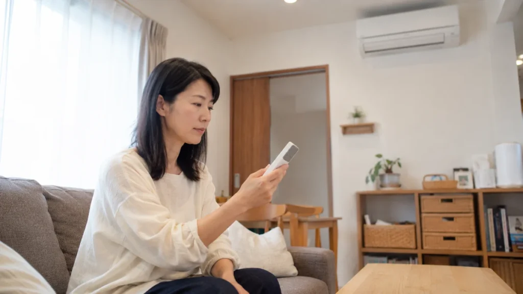 エアコンのリモコンを手に持ち、表示を落ち着いて確認する女性。安全にできる確認の様子