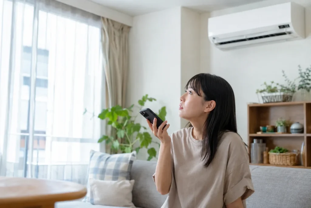 エアコンを止めてスマートフォンで相談しようとする女性。危険サインがあるときは使用を止めて相談する様子