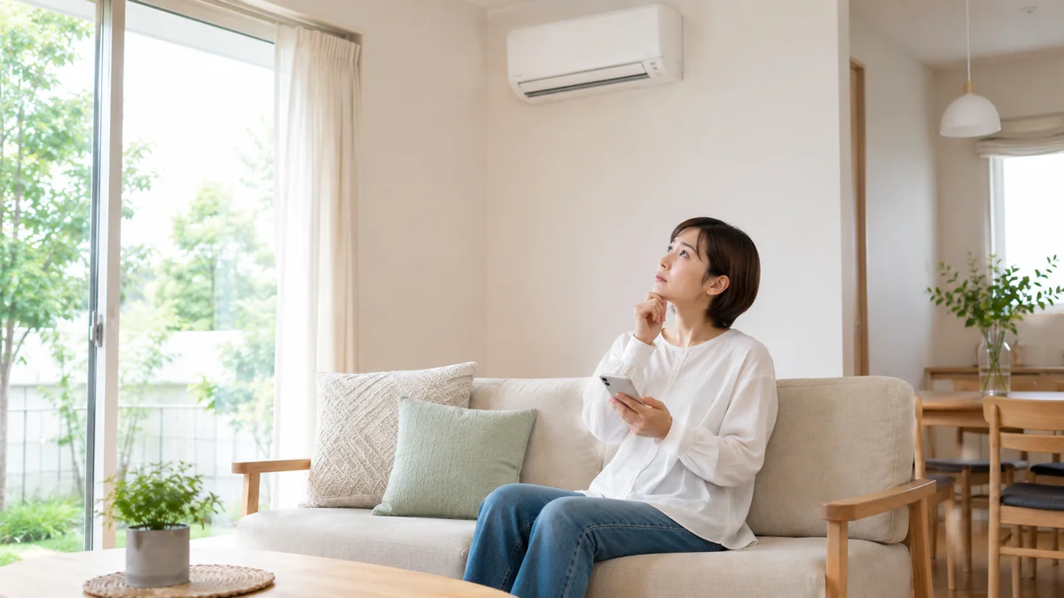 10畳のリビングで壁掛けエアコンを見上げてスマホで検討する女性