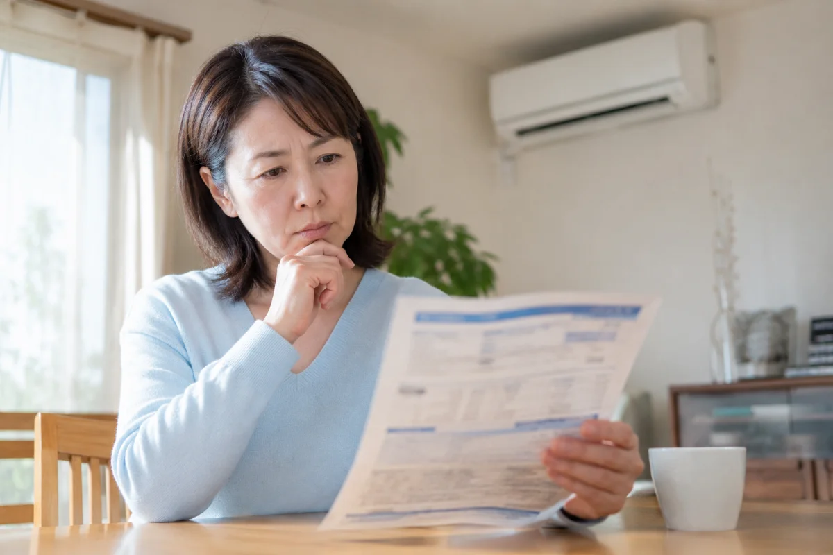 電気料金の明細を手に考え込む女性。エアコンの臭いを放置すると効きや電気代にも影響するイメージ